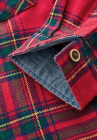 Röd rutigt flanelltyg med gröna och gula accenter; har denimkrage och knapppdetalj; mjuk textur med synlig sömnad.