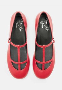 Ballerine in pelle rossa con design a T-strap, caratterizzate da sezioni ritagliate e un'accento con fibbia lateralmente. Interno nero.