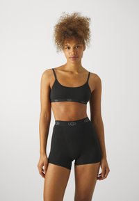Svart bh og høytlivede shorts laget av myk stoff, med UGG-merke på linningen. Enkel, sømløs design med justerbare stropper.