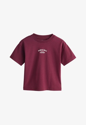 Mørkerød T-shirt med korte ærmer og hvid tekst på brystet, der lyder "Unlimited Smiles Everyday" i et lille buet design.