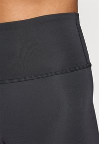 Højtaljede sorte leggings med glat, strækbart stof, der har en fladlock søm ved taljen og en sømløs tekstur.