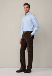 Light blue button-up shirt, brown corduroy pants, and dark shoes. The shirt has a classic collar and the pants have side pockets.