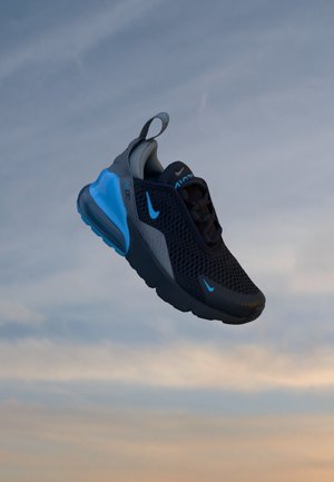 Baskets Nike Air Max 270 noires et bleues avec empeigne en mesh, talon avec coussin d'air et languette, flottant sur un fond de ciel nuageux.
