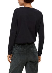 Czarna koszula z długim rękawem i okrągłym dekoltem, w zestawieniu z teksturowanymi, ciemnozielonymi spodniami z sztruksu, które mają pionowe paski i tylne kieszenie.