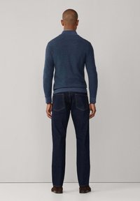 Maglione di lana blu navy con colletto, indossato con jeans scuri, mostrato di spalle su uno sfondo neutro.