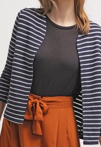 Striped cardigan in navy and white, open front with 3/4 sleeves, worn over a black shirt, paired with an orange skirt featuring a bow tie waist.