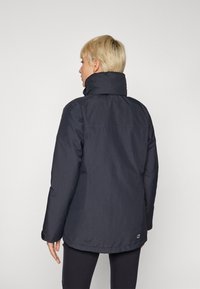 Navy blue insulated jacket with high collar, long sleeves, and a smooth texture. Features a logo detail near the hem, simple design.