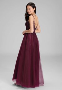 Długa burgundowa suknia z dopasowanym gorsetem, wyszukanym zdobieniem z koralików i zwiewną spódnicą z tiulu. Posiada cienkie ramiączka i głęboki dekolt na plecach.
