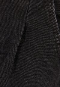 Textura de tela de mezclilla negra con un sutil brillo, que presenta un patrón de tejido diagonal y detalles de costura visibles.