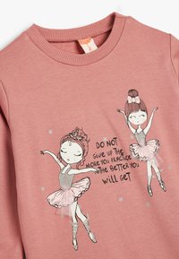 Sudadera de algodón rosa con ilustraciones de dos bailarinas de ballet y acentos de purpurina, y el texto: "NO TE RINDAS..." en letras negras.