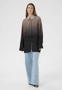 Langærmet skjorte med en gradient fra lys beige til mørkebrun, med krave, knaplukning og løs pasform. Kombinationen er med vide jeans.