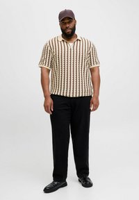 Polo a maniche corte in crema con motivo verticale marrone, colletto beige, abbinato a pantaloni neri e mocassini neri.