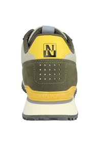 Zapatilla deportiva verde y beige con un acento amarillo, materiales sintéticos y ante texturizado, logo prominente y detalles perforados en el talón.