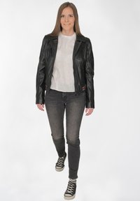 Schwarze Leder-Bikerjacke mit Reißverschlussdetails, getragen über einem hellen Leinentop und dunkelgrauen Skinny-Jeans. Schwarze Sneaker runden das Outfit ab.