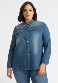 Jeansowa koszula z guzikami w średnim niebieskim kolorze, z kołnierzykiem, dwiema kieszeniami na piersiach i złotymi akcentami. Długie rękawy z detalami mankietów.