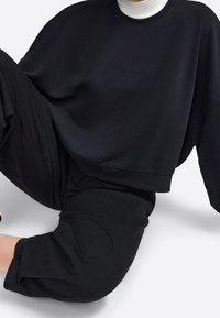 Svart oversized sweatshirt i mjuk tyg, med rund halsringning och sänkta axlar, i kombination med matchande svarta tapered byxor.