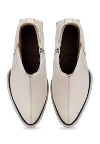 Bottines beiges en cuir, avec un bout pointu, une fermeture éclair latérale et une bordure contrastante noire le long de la semelle.