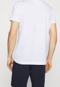 Camiseta de algodón blanca con cuello redondo y mangas cortas, con un diseño liso y un corte relajado. La vista trasera muestra una textura suave y costuras.