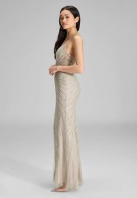 Długa, dopasowana suknia z beżowego materiału z akcentami z srebrnych koralików. Posiada dekolt w serek i diagonalny wzór pasków, sięgający do podłogi.