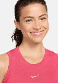 Top atletico senza maniche di colore rosa realizzato in tessuto a coste. Presenta un colletto rotondo e un piccolo logo Nike bianco centrato sul petto.