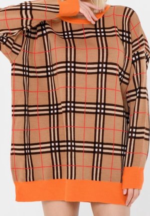 Beige sweaterkjole med sort, hvid og rød ternet mønster, med lyse orange manchetter og kant, båret af person, der dækker ansigtet med armen.