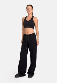 Sutien sport negru cu un design simplu, asociat cu pantaloni de trening largi de culoare neagră, cu talie elastică și detaliu cu logo.