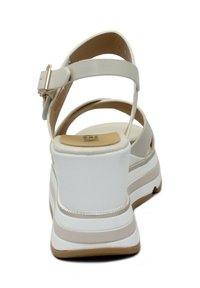 Witte patenten leren sandaal met een brede band en verstelbare gesp, gevoerd voetbed en chunky witte hak met beige accenten.