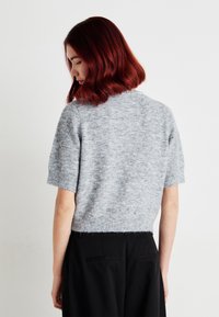 Šedý svetr s krátkým rukávem, měkkou strukturou a mírně roztrhaným lemem, s kulatým výstřihem a minimalistickým designem.