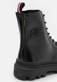 Svarta läderankelstövlar med en rund logopatch, texturerad sula och ett dragband med röda och blå ränder bak.