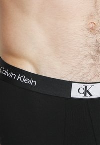 Juodi Calvin Klein boxerių šortai pasižymi lygia medžiaga su juodu elastingu juosmeniu, kuriame yra baltas prekės ženklas ir logotipas.