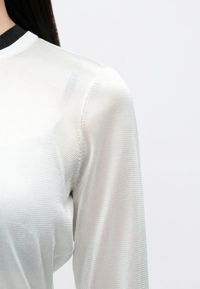 Haut blanc léger à manches longues avec tissu texturé, doté d'un col côtelé noir. Le matériau semble transparent avec un léger éclat.