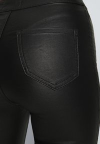 Närbild av svarta läderbyxor med synlig stygn på bakfickan på en person.