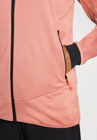 Heled roosa lukuga jakk mustade aktsentidega, millel on tekstuurne kangas, küljetasku kontrastse lukuga ja istuvad mansetid.