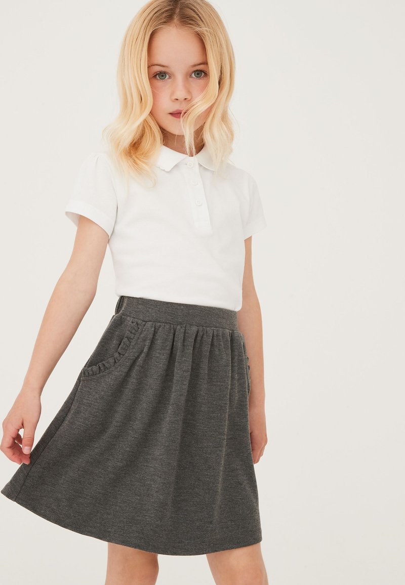 Polo bianco a maniche corte, abbinato a una gonna grigia con tasche arricciate e una vita elastica, dalla texture liscia.