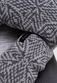 Strikket sweatermanchet med et geometrisk mønster i nuancer af grå, med en glat tekstur og et sort mærke syet ind i stoffet.