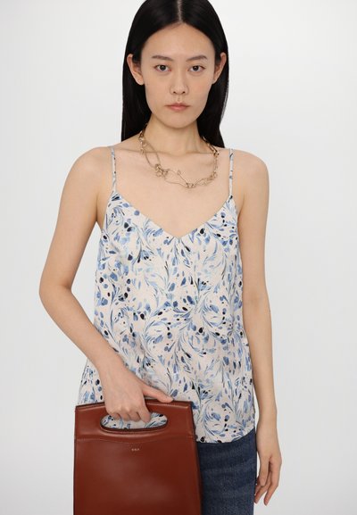 Light blue and cream floral patterned camisole with thin straps; model holds a brown leather handbag with a cut-out handle.