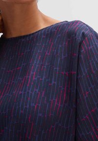 Marineblauwe top met een rechthoekig patroon in roze en paarse tinten. Zachte stof met een boothals en gedrapeerde mouwen. Textuurdetails op het oppervlak.