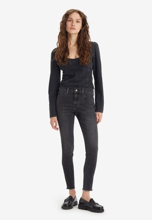 Schwarze schmal geschnittene Jeans aus Denim mit hoher Taille und abgefallenem Saum, kombiniert mit einem figurbetonten Langarmoberteil in einem passenden dunklen Farbton.