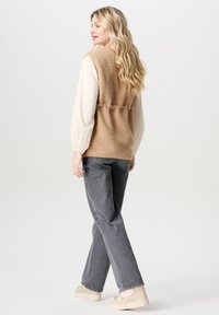 Tan fleeceväst med mjuk textur, vit långärmad skjorta under, grå raka jeans och beige plattformssneakers.