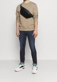 Bolso bandolero negro, sudadera beige, vaqueros azules y zapatillas multicolores. Incluye características como una superficie de bolso texturizada y puños enrollados en los vaqueros.