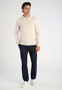 Beige långärmad polo med dragkedja, kombinerad med marinblå byxor och vita sneakers. Mjuk textur, minimalistisk design.