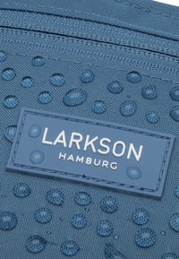 Kék szövet tasak vízcseppekkel, téglalap alakú címkével, amelyen fehér szöveggel a "LARKSON HAMBURG" felirat található, illeszkedő kék keretben.