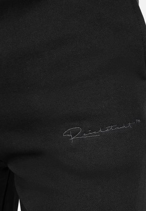 Pantaloni della tuta neri realizzati in tessuto morbido, con un logo ricamato in un colore contrastante, posizionato vicino al lato inferiore.