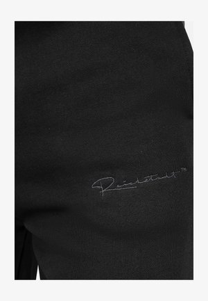 Zwarte sweatpants van zachte stof met een geborduurd logo in een contrasterende kleur, gepositioneerd nabij de onderzijde.