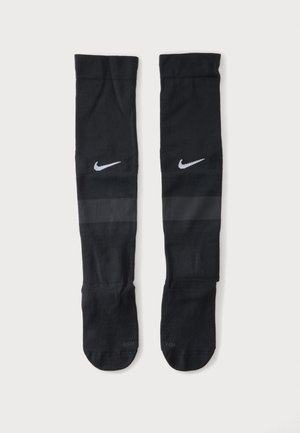 Pár čiernych Nike športových ponožiek po kolená so sivými pruhmi a bielymi logami Swoosh, položených na bielom pozadí.