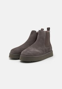 Grå mocka chelseaboots med elastiska sidopaneler, rund tå och kraftiga gröna gummisulor. Har en lätt klack och dragöglor.