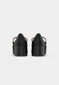 Black heeled sandals made from smooth leather, featuring an open back, adjustable strap with gold hardware, and a chunky heel.