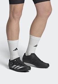 Black cycling shoes with a sleek design, featuring a textured upper, silver stripes, and a dial lacing system, paired with white socks.