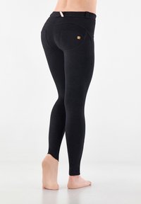 Leggings neri con vita alta, texture liscia e cuciture a contrasto. Presentano una tasca posteriore curva con dettaglio in logo dorato.