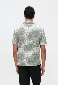 Trumpomis rankovėmis marškiniai su šviesiai pilku ir juodu abstrakčiu raštu, austu audiniu ir plyšiu ant apykaklės. Galinės pusės vaizdas.